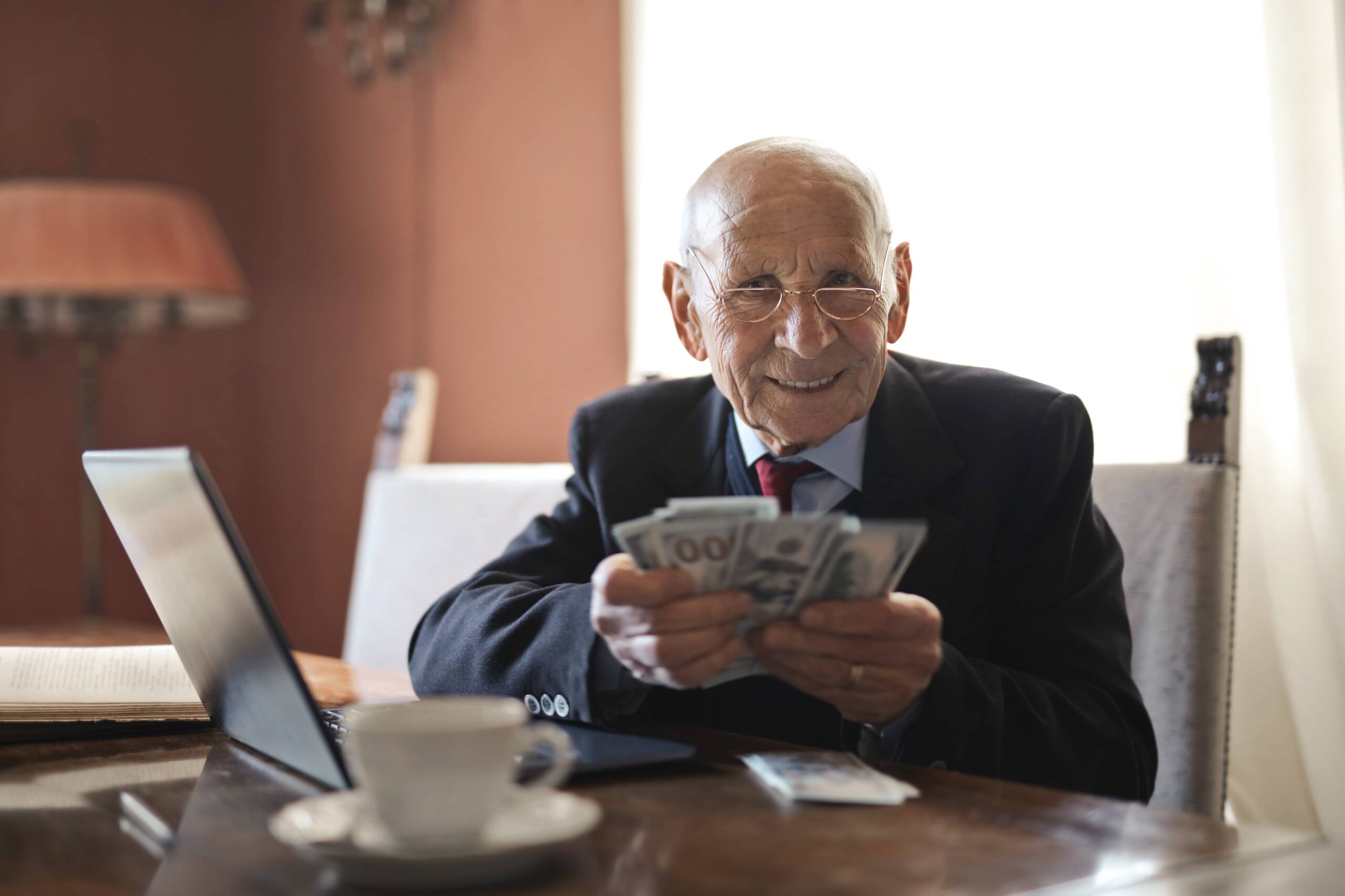 Starszy mężczyzna w okularach siędzący przy biurku z pieniędzmi. Autozapis do PPK