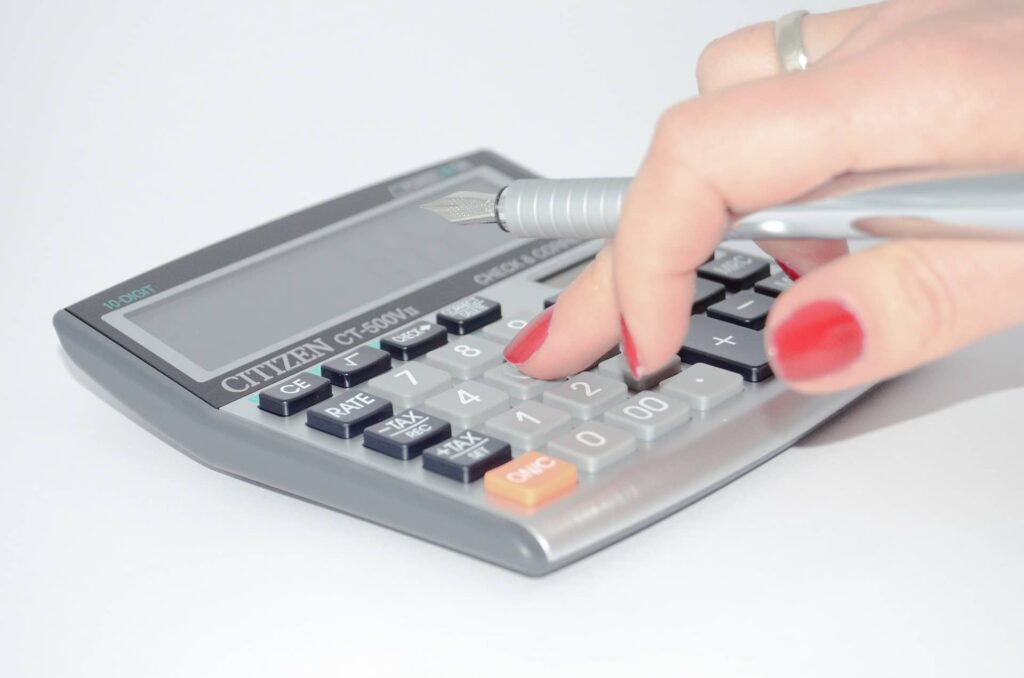 Kobieca dłoń trzymająca pióro i obliczająca coś na kalkulatorze (kiedy zarząd spółki może skorzystać z kwoty wolnej)