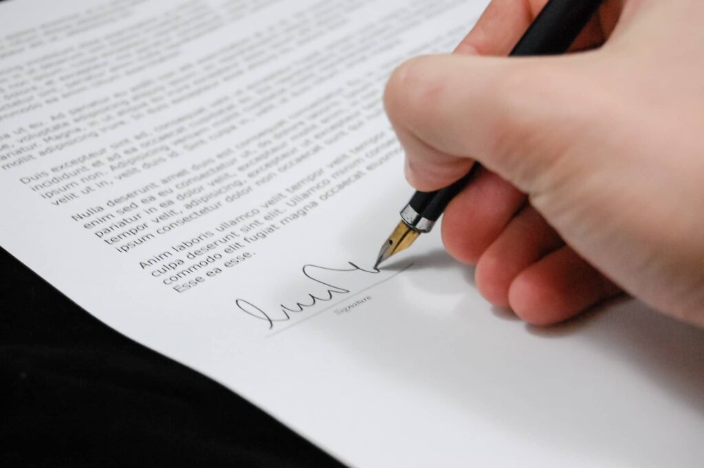 Dłoń trzymająca pióro i składająca podpis na dokumencie (umowa o dzieło z własną spółką)