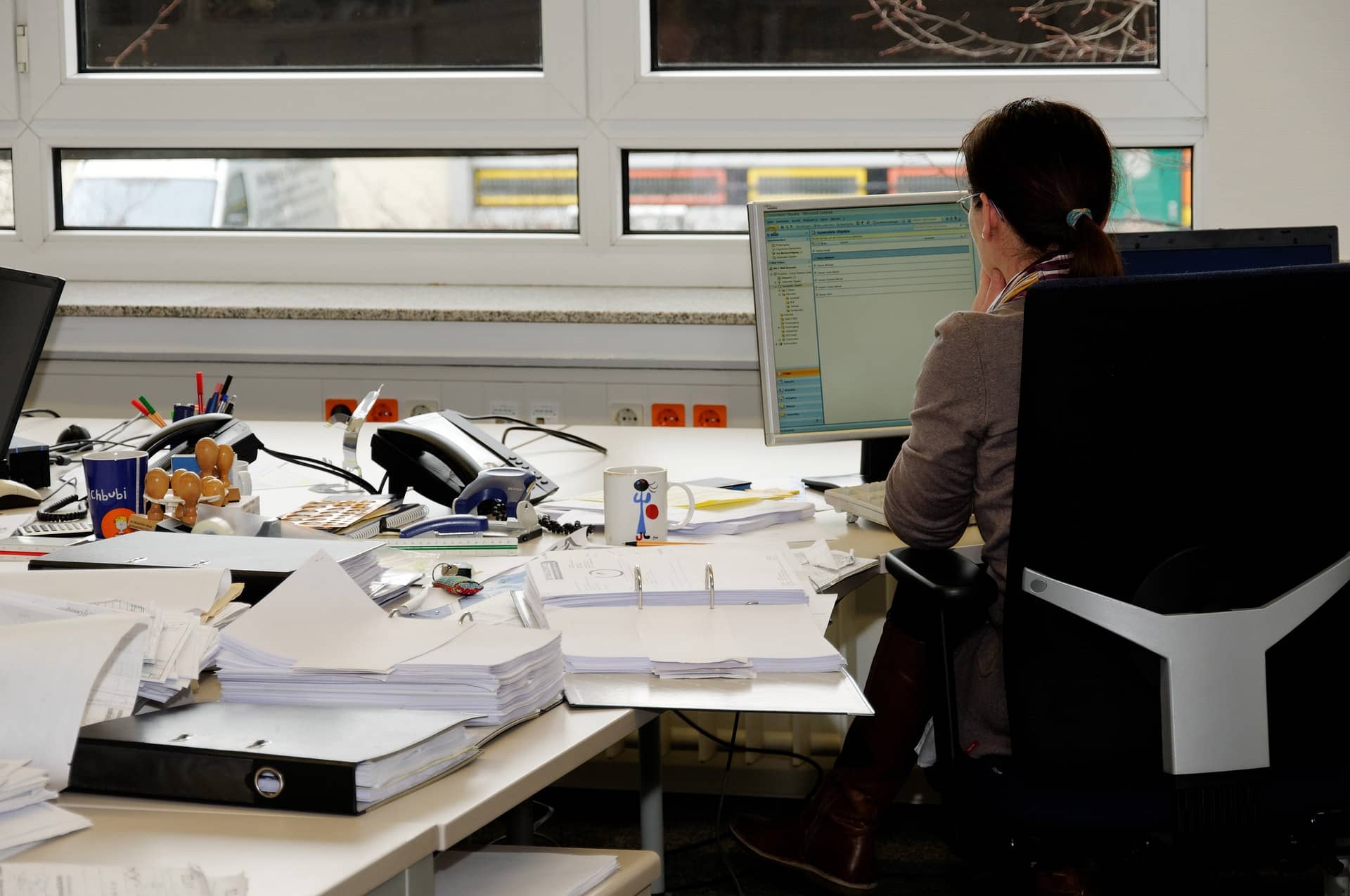 siedząca przy komputerze kobieta oraz biurko z licznymi dokumentami (spółka z o.o. bez pracowników)