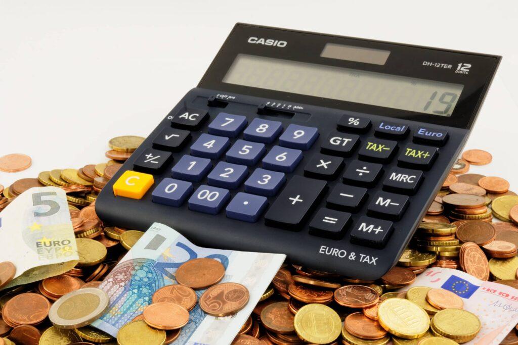 Stos pieniędzy (banknoty i monety) a na nich leżący kalkulator (zatrudnianie członka zarządu bez wynagrodzenia)