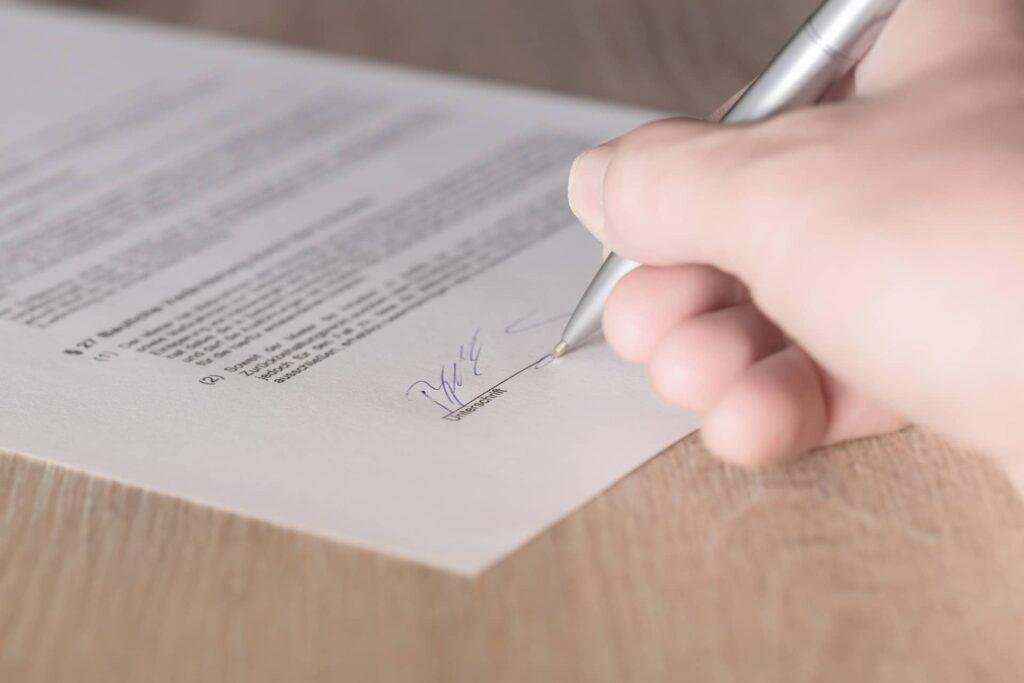 Widoczna dłoń z długopisem, podpisująca dokument (spółka z o.o. w organizacji)