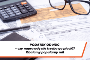 Dokumenty podatkowe, kalkulator i okulary na biurku – grafika ilustrująca temat „Podatek od NDG – czy naprawdę nie trzeba go płacić?”